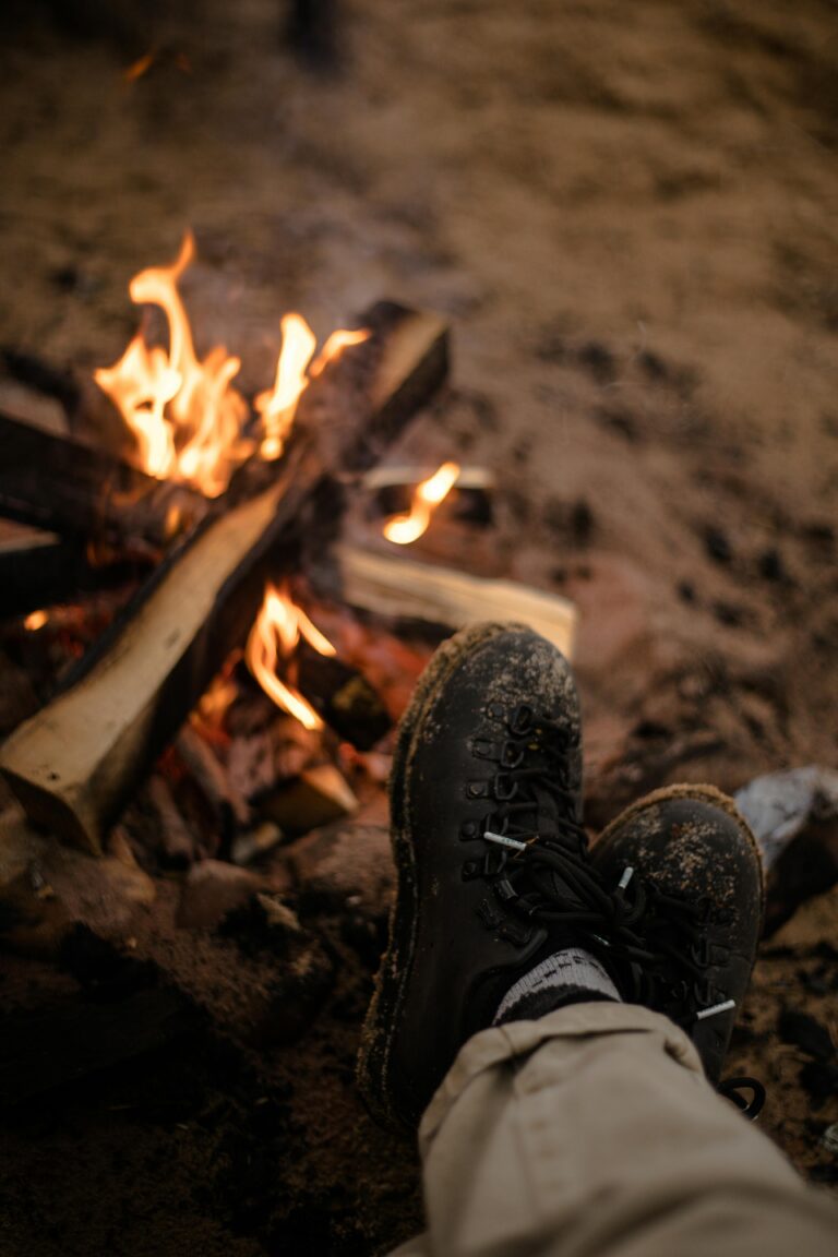 Experience the cozy warmth of a campfire with boots resting nearby, perfect for outdoor adventures.